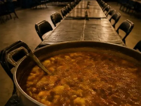 Olla grande de guiso sobre una mesa larga del salón del club con guirnaldas de luces